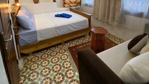 Un dormitorio con una cama de madera, una mesita pequeña, un tapete decorativo, una ventana con cortinas y una lámpara colgante.