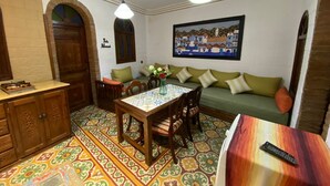 Una sala de estar acogedora con piso estampado, una mesa de comedor con sillas, un sofá con cojines y un cuadro en la pared.
