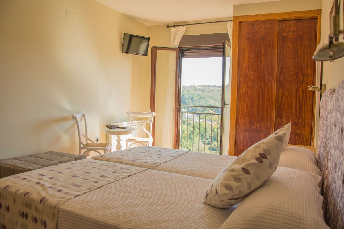 A bedroom with two beds, a small table, a chair, a TV, and a balcony with a view.