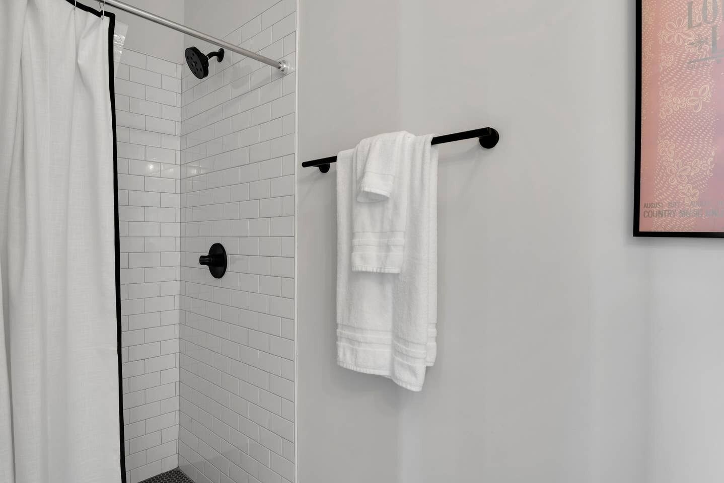 Une salle de bain avec des murs carrelés de carreaux blancs, une douche avec une porte en verre et un porte-serviettes avec deux serviettes blanches.