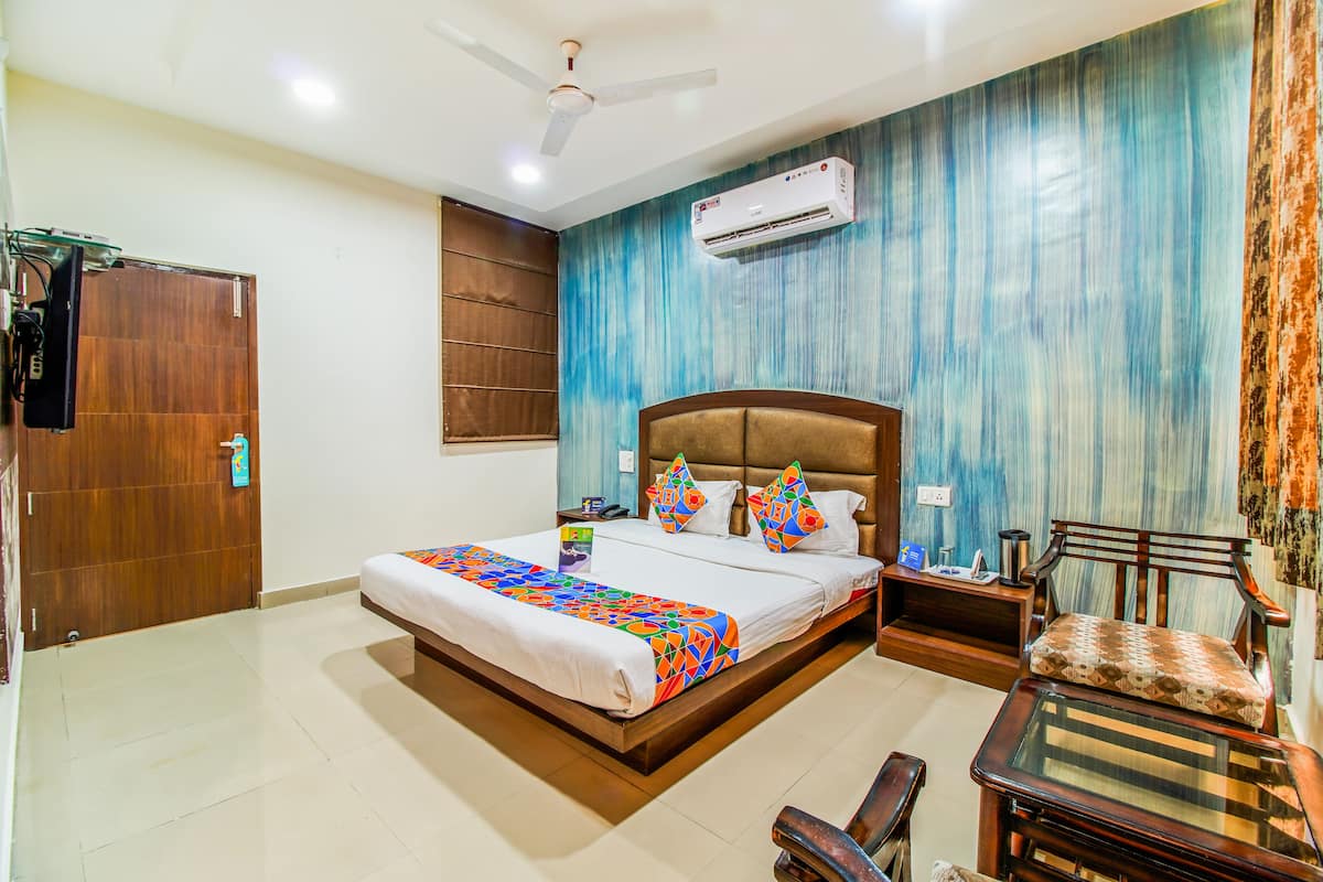 A hotel room with a large bed, a wooden headboard, a nightstand, a chair, and an air conditioning unit on the wall.