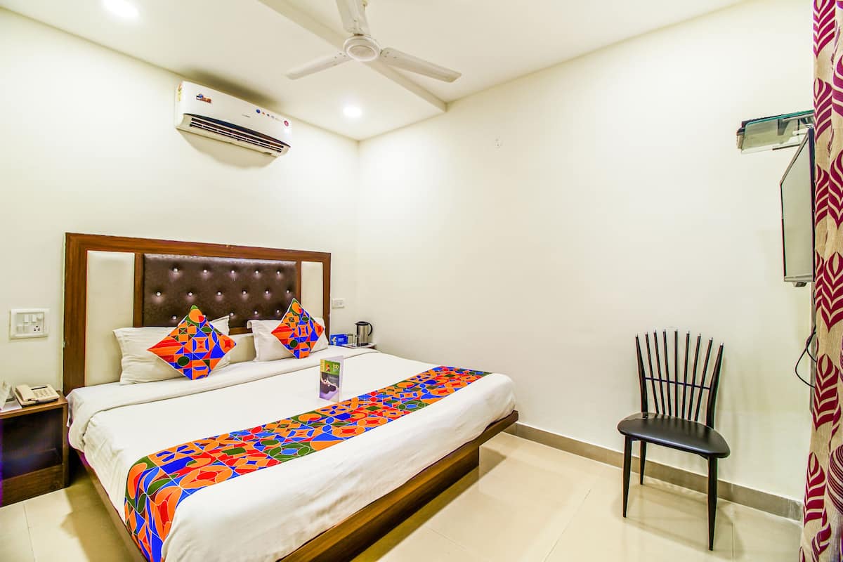A hotel room with a bed, a chair, an air conditioning unit, and a ceiling fan.