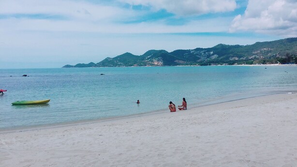 A beach with clear water, a few people, and a green boat. - Oimho Beach House Apartment Beach Front (Koh Samui)