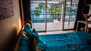A room with a large sliding glass door leading to a balcony with a view of palm trees and a body of water. - Oimho Beach House Apartment Beach Front (Koh Samui)