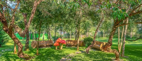 Un exuberante jardín con un banco de piedra, un tronco de madera y una escultura de hongo.