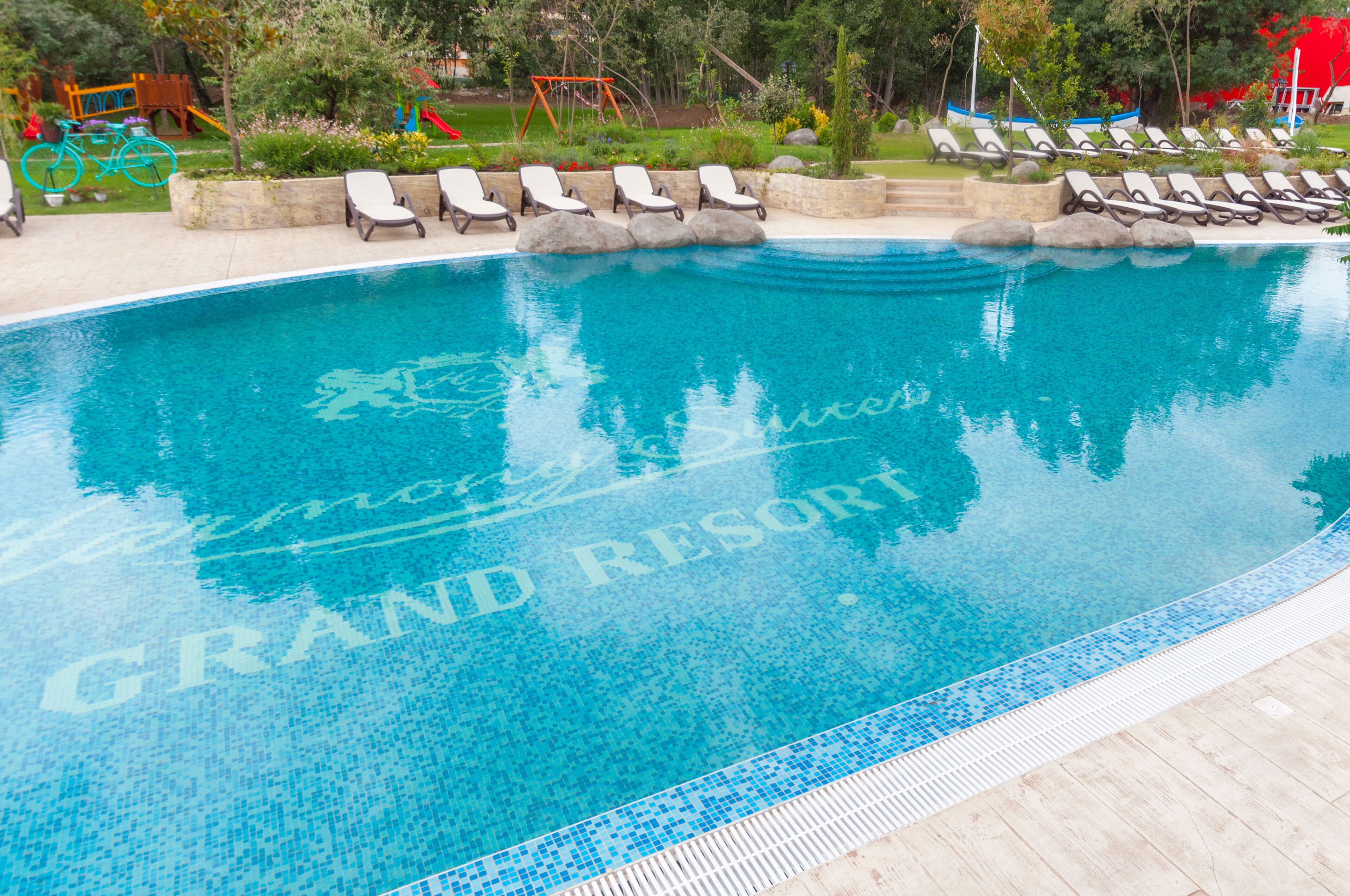 A clear swimming pool with lounge chairs and a children's play area in the background.