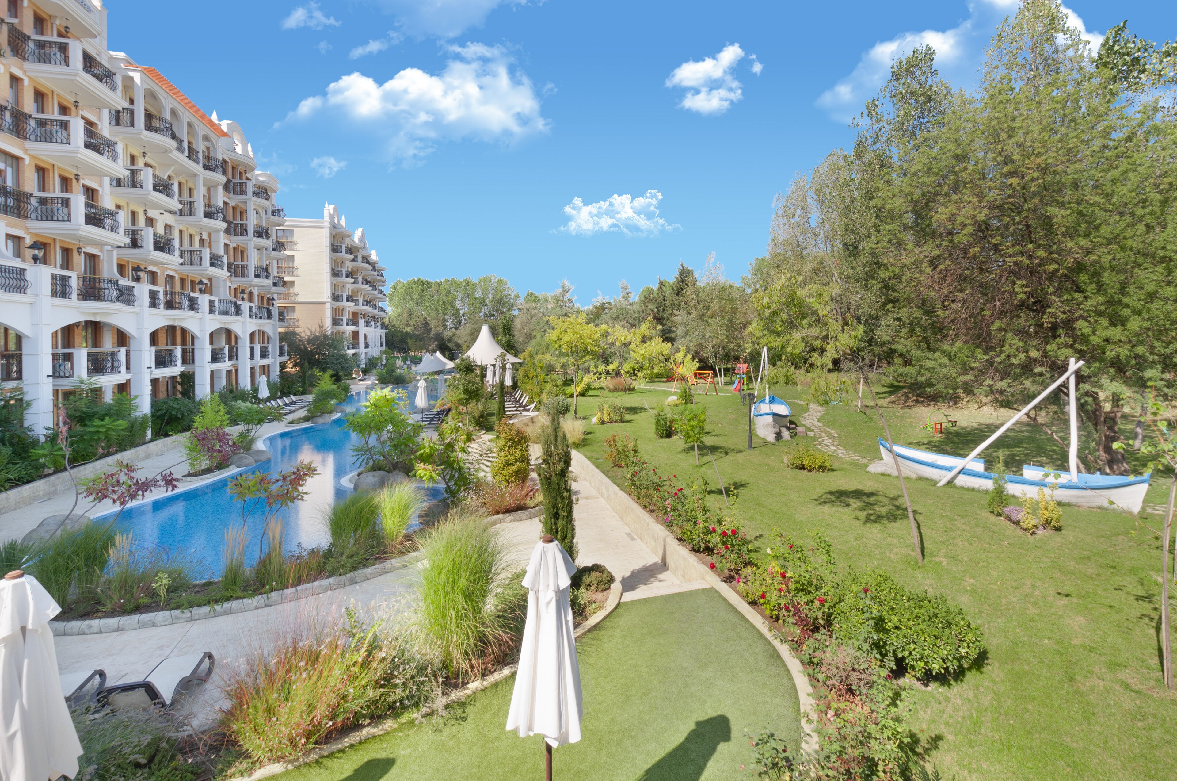 A hotel with multiple balconies, a swimming pool, and a well-maintained garden with a gazebo.