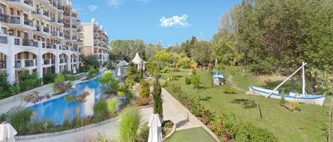 A hotel with multiple balconies, a swimming pool, and a well-maintained garden with a gazebo.