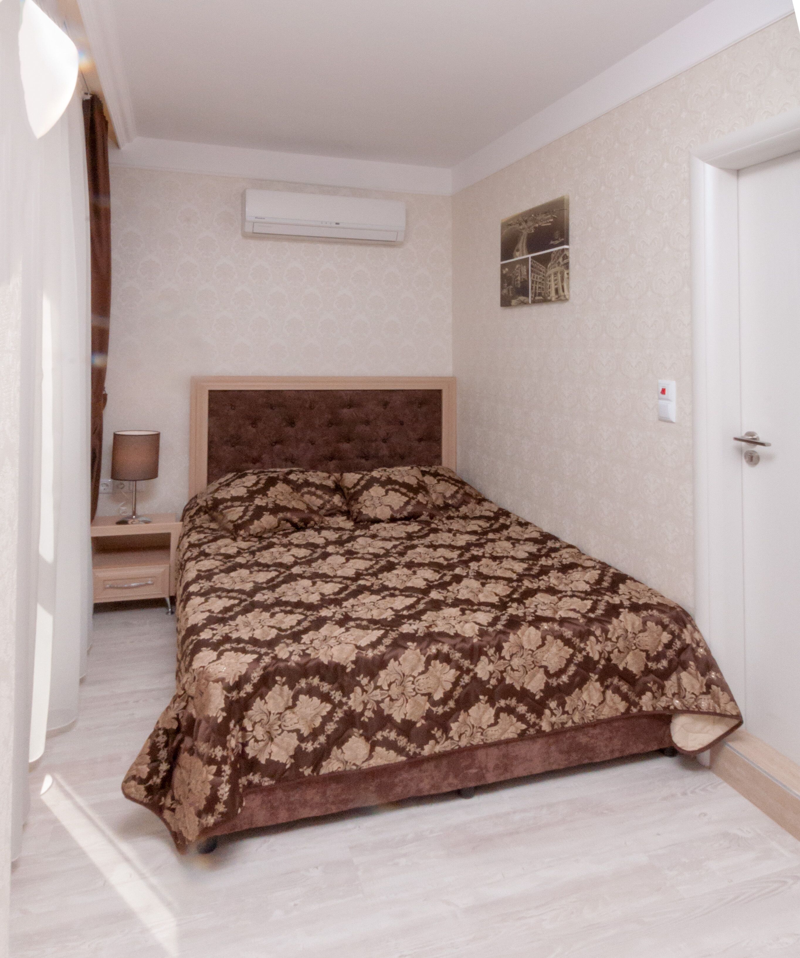 A bedroom with a bed, a nightstand, a lamp, an air conditioning unit, and a door.