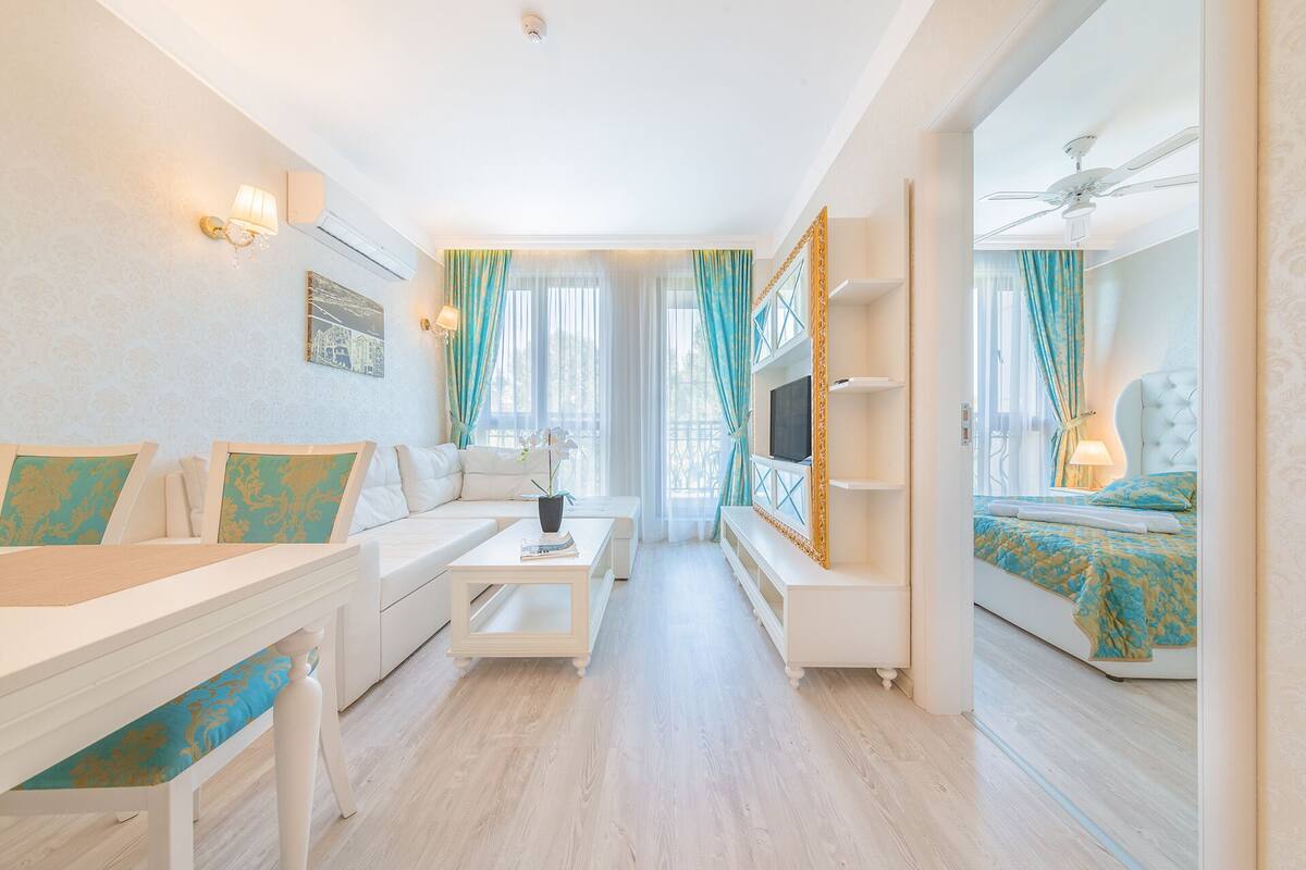 Una habitación de hotel moderna con sofá, una mesita, televisor y cama con cubrecama azul y dorado.