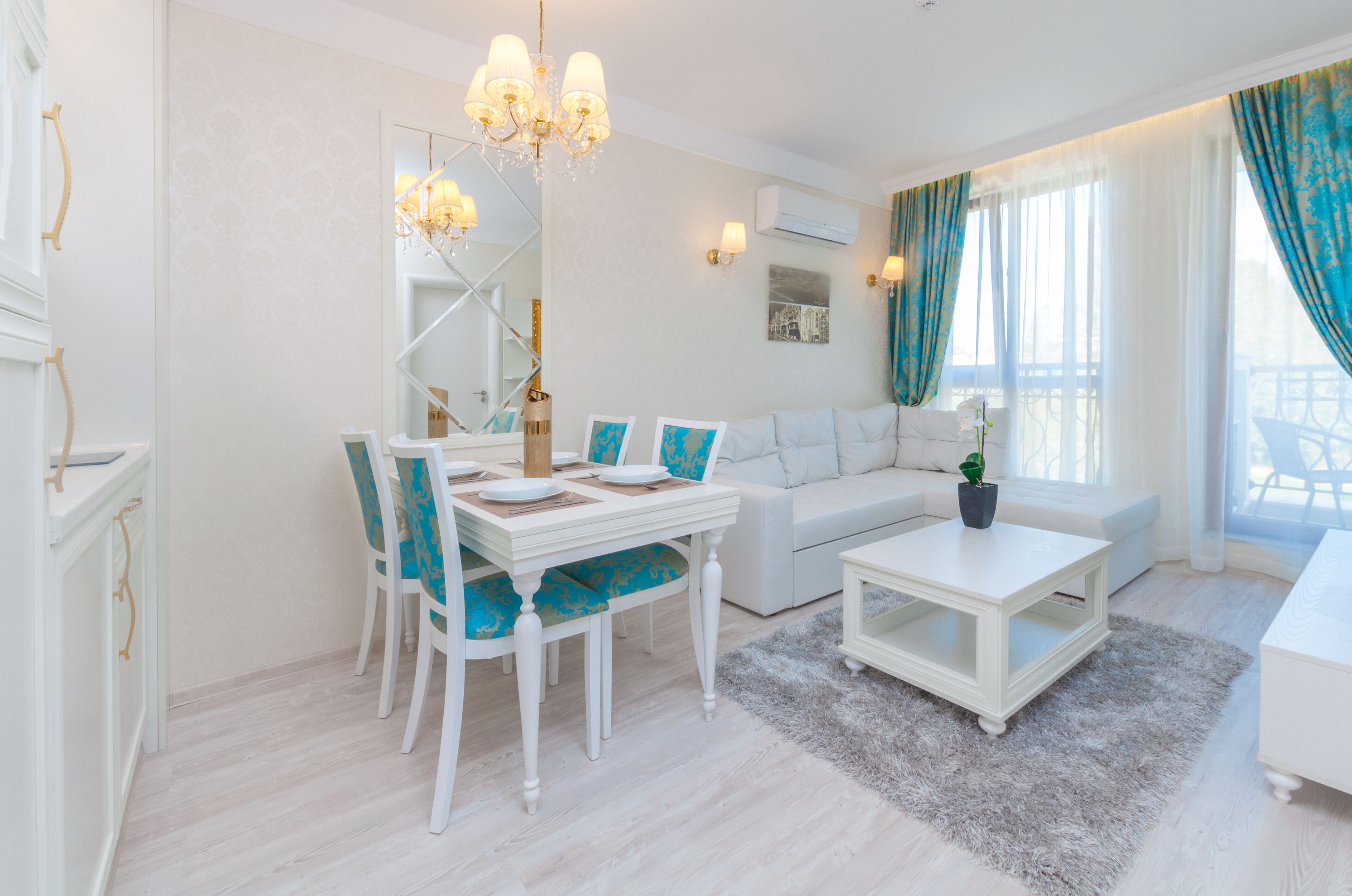Un salon moderne comprenant un coin repas, des meubles blancs, un lustre et une grande fenêtre agrémentée de rideaux.