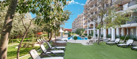 A hotel courtyard with a swimming pool, sun loungers, and a well-maintained lawn.