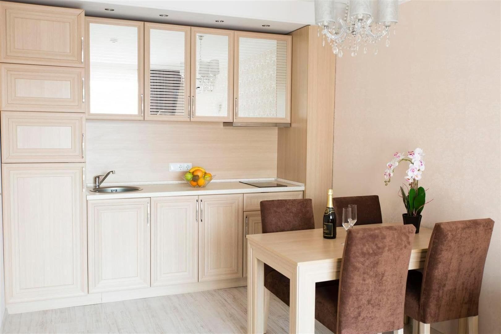 A modern kitchen with light wood cabinets, a built-in oven, and a dining area with a table and chairs.
