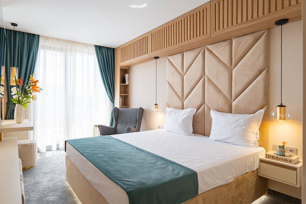 Una habitación de hotel moderna con una cama grande, una silla, una mesita de noche y una mesilla auxiliar.