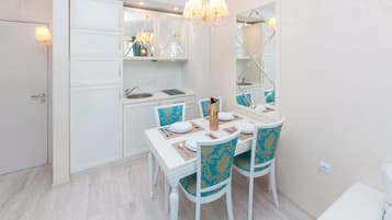 Un espace repas moderne avec une table blanche dressée pour quatre personnes, des chaises bleues ornées de motifs dorés, un lustre et un grand miroir au-dessus de la table.