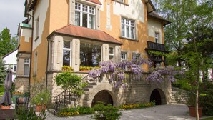 A historic building with a stone archway, a balcony with purple flowering vines, and a paved courtyard with potted plants. - Gästehaus Musmann (Hann. Muenden)