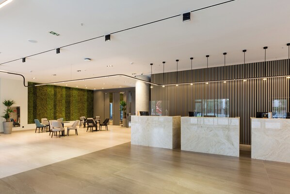 A modern reception area with marble counters, a green vertical garden, and a seating area with chairs and tables.
