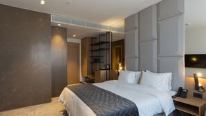 Quarto de hotel moderno com uma cama grande, mesa de cabeceira com telefone e prateleira fixa na parede.