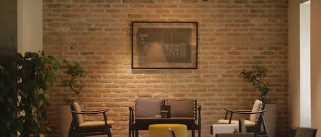 A cozy seating area with a brick wall, framed artwork, and potted plants.