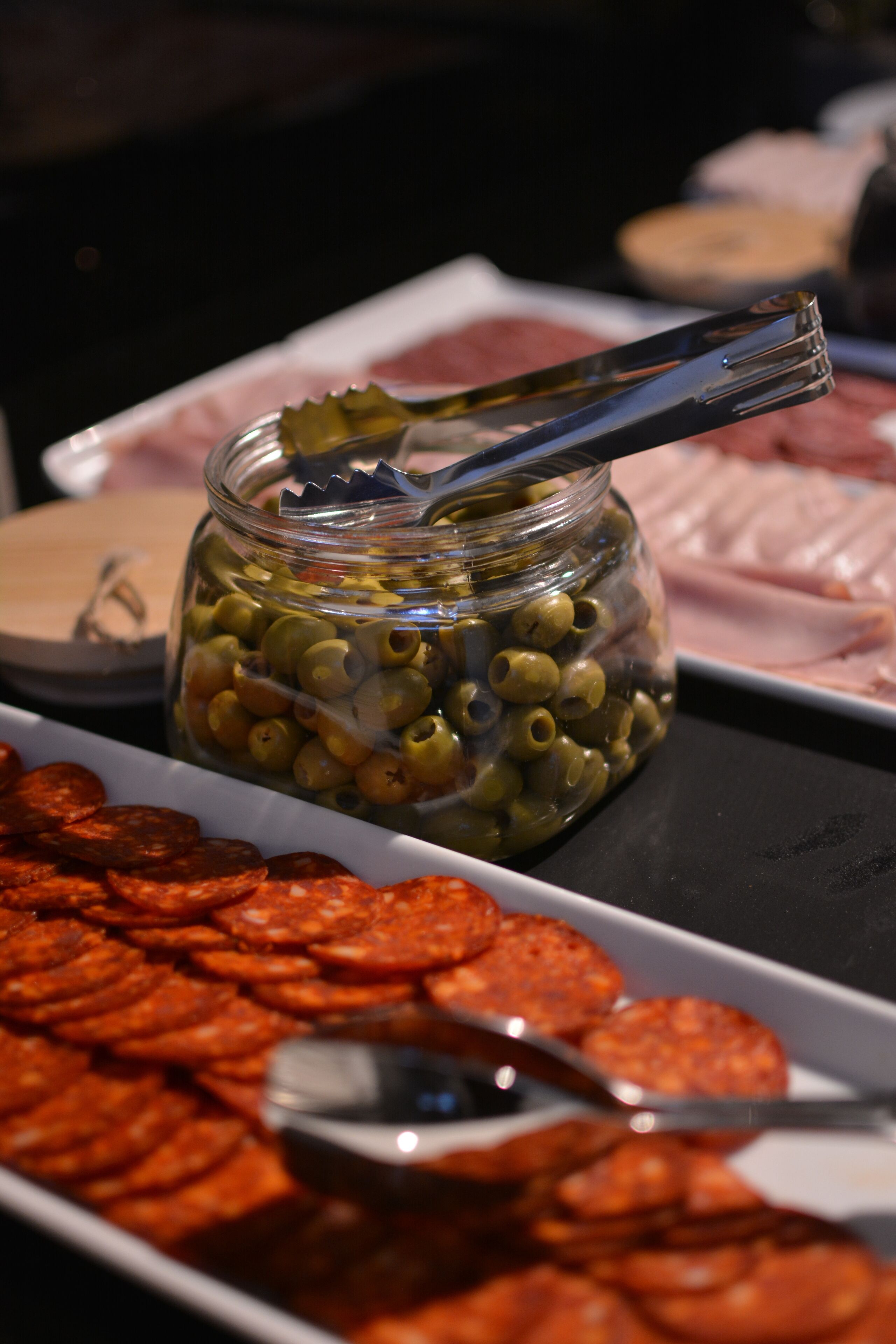 A buffet with a jar of olives and a plate of sliced salami.
