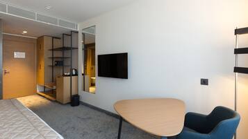 A modern hotel room with a bed, a desk, a chair, a TV, and built-in shelving.