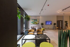 A modern lobby with a seating area, a TV screen, and potted plants. - Hotel Mona Plaza (Belgrade)