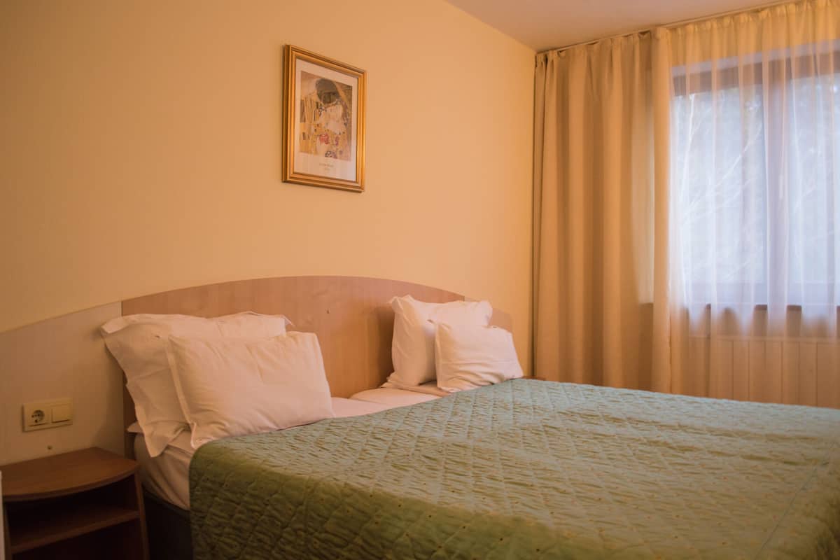 Une chambre d’hôtel avec un lit, une table de chevet, un tableau encadré au mur et une fenêtre avec des rideaux.