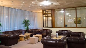 A modern living room with leather sofas, wooden coffee tables, and a large window with blinds. - Hotel Edelweiss (Samokov)
