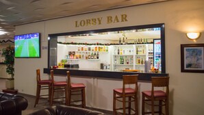 A bar area with a counter, bar stools, and a television displaying a sports game. - Hotel Edelweiss (Samokov)