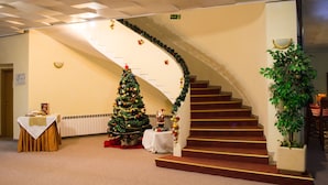 A staircase with a Christmas tree and decorations, a table with a white tablecloth, and a potted plant. - Hotel Edelweiss (Samokov)
