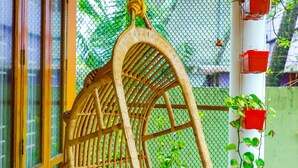 Una silla colgante de mimbre con fondo de malla, un pilar blanco con macetas rojas y una planta verde.
