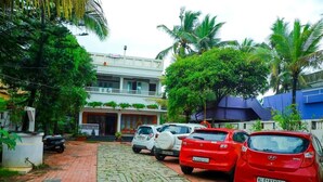 Un edificio de dos pisos con balcón, coches aparcados y palmeras.