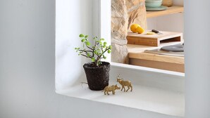 Una ventana, un muro de piedra, una planta en maceta y un estante con utensilios de cocina.