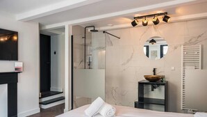 Ein modernes Badezimmer mit einer begehbaren Glasdusche, einem runden Spiegel und einem Aufsatzwaschbecken.