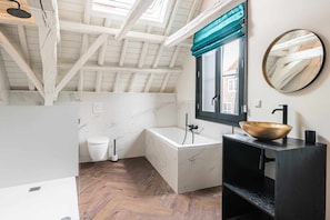 A modern bathroom with a freestanding bathtub, a large mirror, and a window with a view of the outside.