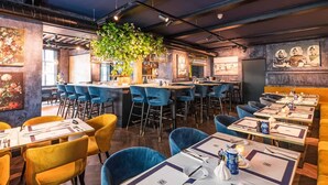 Ein Restaurant mit Barbereich, blauen Barhocker und Esstischen.