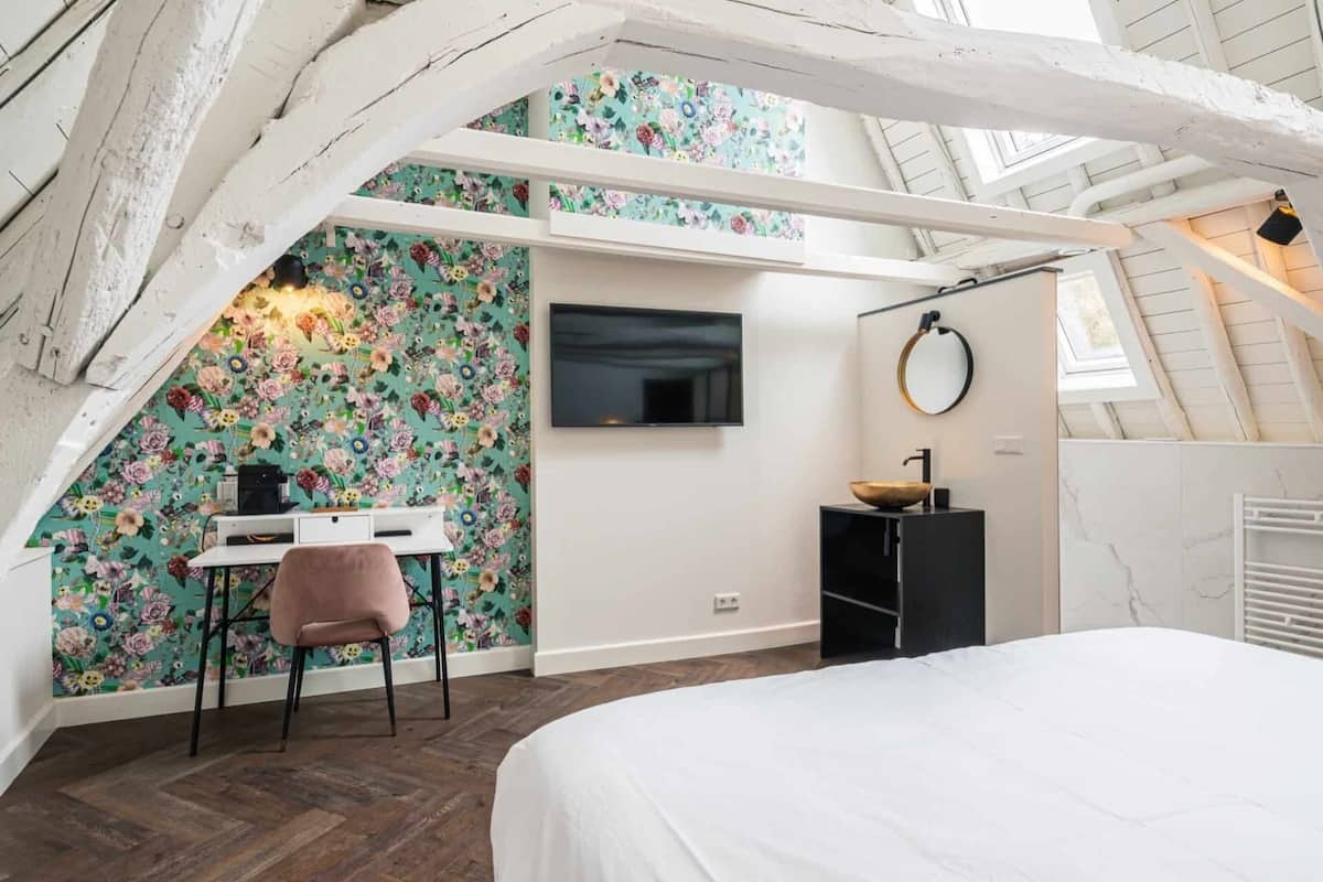 Ein Schlafzimmer mit einem Bett, einem Schreibtisch mit Stuhl, einem Fernseher, einem Spiegel und einem Badezimmer mit Waschbecken und Handtuchhalter.
