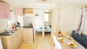 A compact kitchen with a dining area, a bed, and a small living space. - Happy Camp in Camping Bella Italia (Peschiera del Garda)