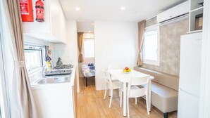 A compact kitchen with a gas stove, sink, and a dining area with a table and chairs. - Happy Camp in Camping Bella Italia (Peschiera del Garda)