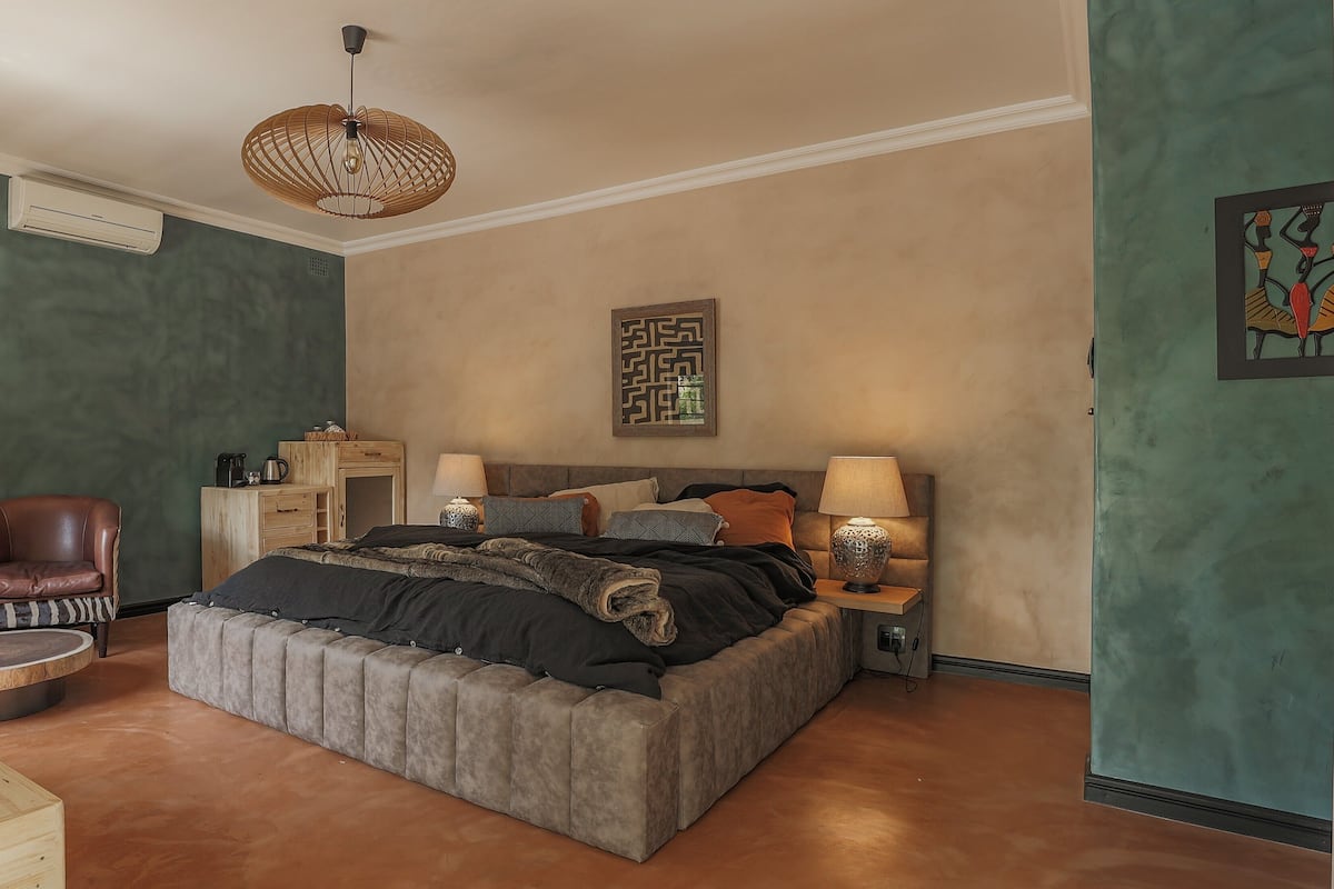 Une chambre à coucher avec un grand lit, deux tables de chevet, une chaise et un luminaire suspendu.