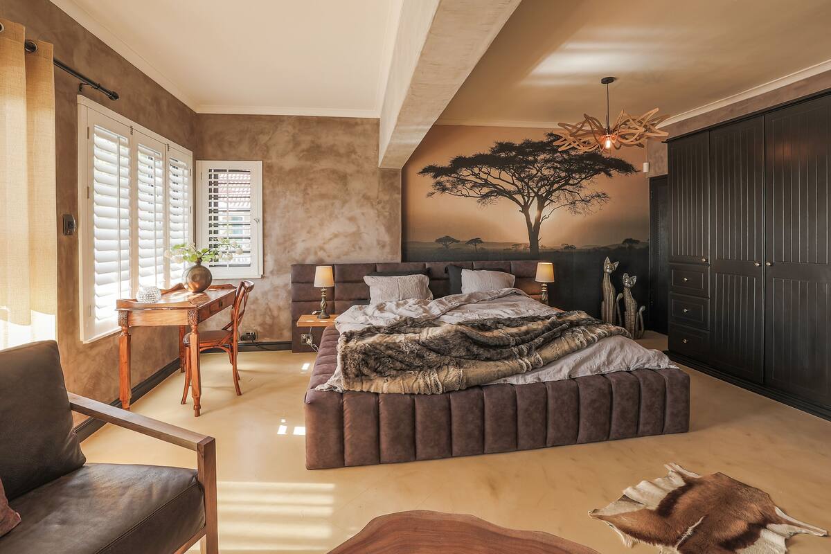 Une chambre avec un grand lit, un bureau et une chaise. On y trouve également une armoire et une fenêtre avec des stores.