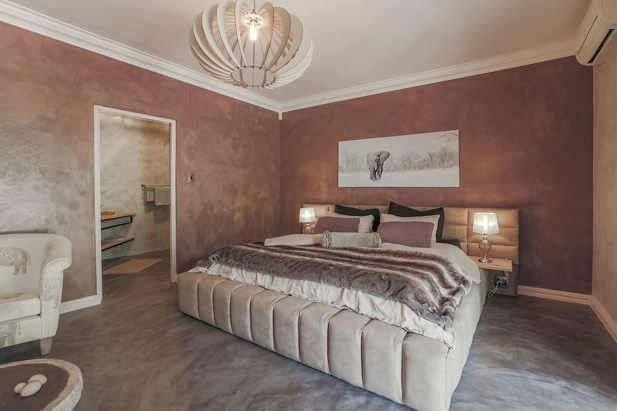 Une chambre avec un grand lit, deux lampes de chevet, un luminaire au plafond, un tableau au mur et une chaise.