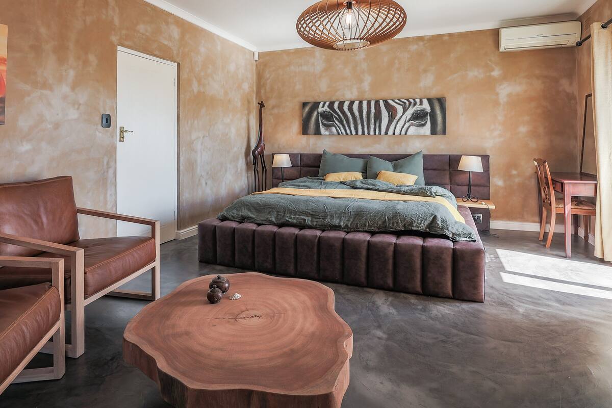 Une chambre moderne avec un grand lit, une table basse en bois, un fauteuil en cuir et un tableau représentant une zèbre accroché au mur.