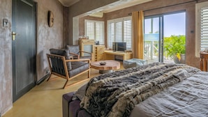 Une chambre moderne avec un grand lit, un bureau et une chaise. Une porte-fenêtre coulissante donne accès à un balcon offrant une vue sur la verdure.