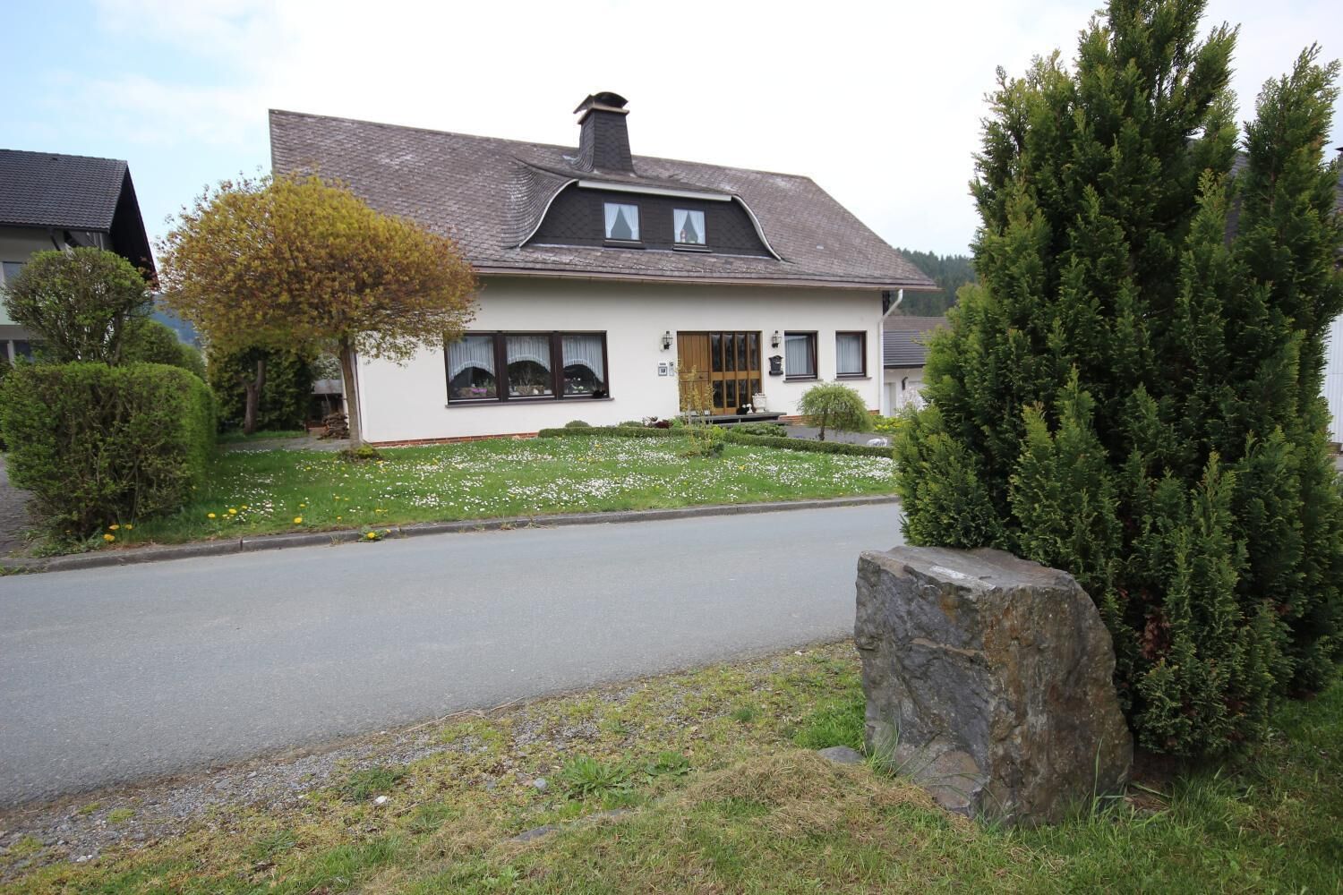 Une maison à deux étages avec un toit en pente, un porche à l’avant et un mur en pierre.