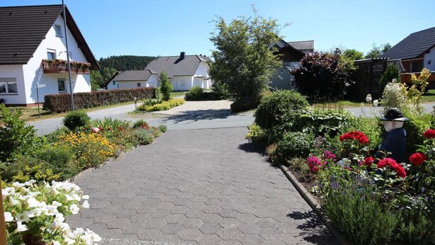 Una calle residencial con casas, una acera pavimentada y macizos de flores.