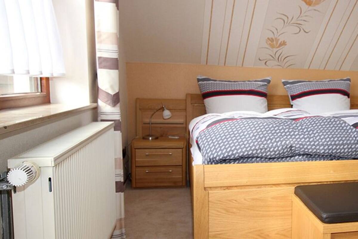A bedroom with a wooden bed, two bedside tables, a radiator, and a window with curtains.