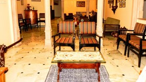 Un interior tradicional con suelo de mármol, una mesa central con mantel estampado y varias sillas tapizadas con diseño a rayas.