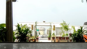 Vista de un patio con macetas, una pared blanca y un edificio al fondo.