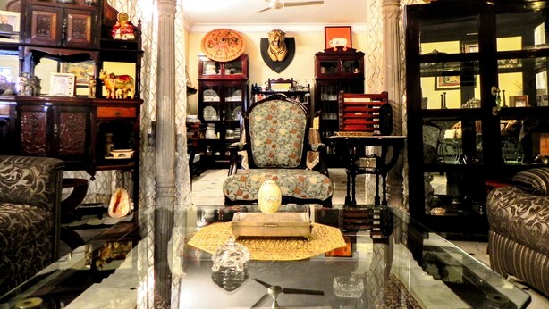 Una sala de estar tradicional con un sofá, sillones, una mesa de centro y una chimenea. Hay objetos decorativos y un reloj en la pared.